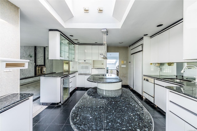 kitchen with sink, a kitchen island, dark stone countertops, oven, and white cabinets