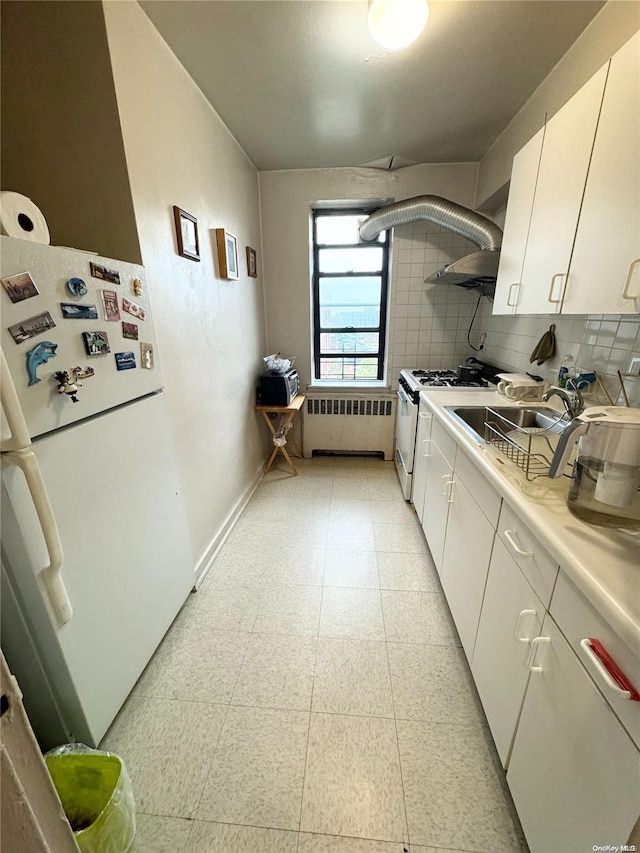 kitchen with radiator, white appliances, wall chimney range hood, sink, and white cabinets