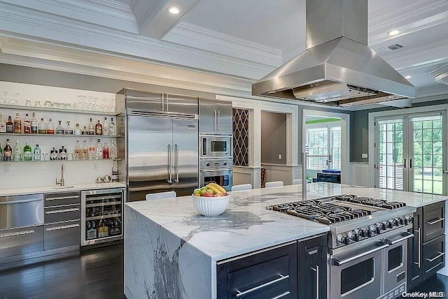 kitchen featuring light stone countertops, wine cooler, built in appliances, island range hood, and a kitchen island