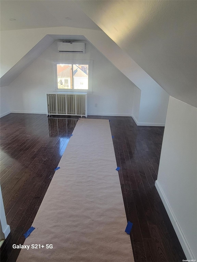 additional living space with an AC wall unit, dark wood-type flooring, and vaulted ceiling