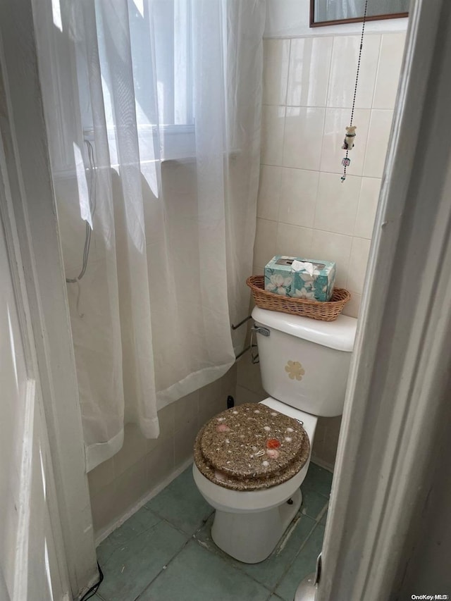 bathroom with toilet, tile patterned floors, and tile walls