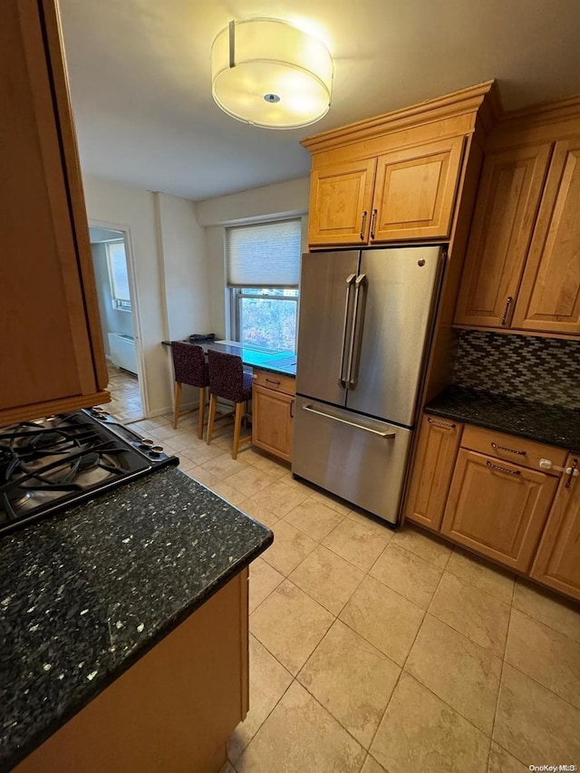 kitchen with stainless steel fridge, backsplash, black gas stovetop, dark stone counters, and light tile patterned flooring