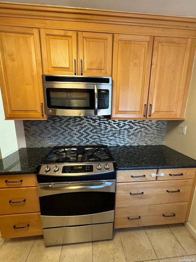 kitchen with decorative backsplash, light tile patterned floors, stainless steel appliances, and dark stone countertops