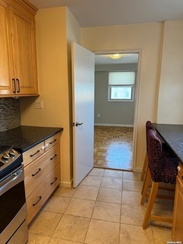 kitchen with decorative backsplash, light tile patterned flooring, stainless steel electric range oven, and dark stone counters