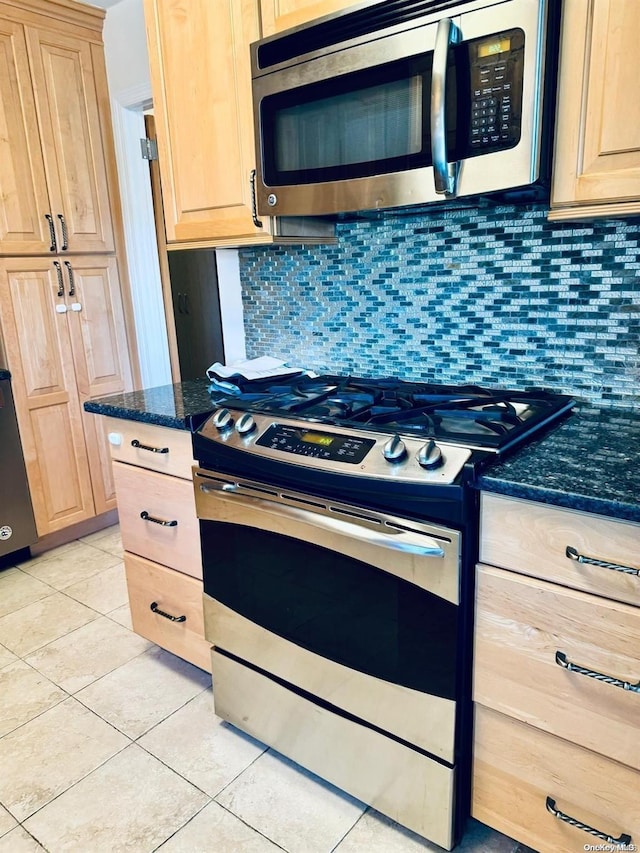 kitchen featuring light brown cabinets, dark stone countertops, light tile patterned floors, appliances with stainless steel finishes, and tasteful backsplash