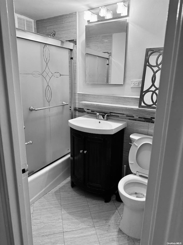 full bathroom featuring vanity, shower / bath combination with glass door, tile patterned floors, toilet, and tile walls