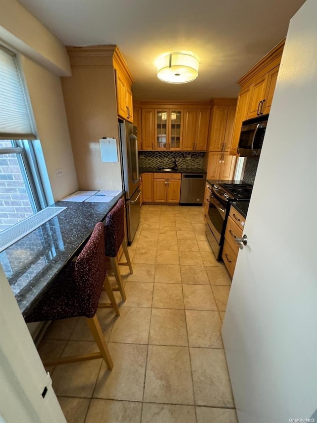 kitchen with backsplash, sink, dark stone countertops, light tile patterned flooring, and stainless steel appliances