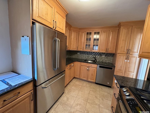 kitchen with sink, stainless steel appliances, dark stone countertops, decorative backsplash, and light tile patterned floors