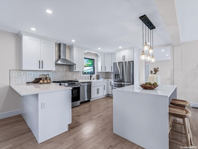 kitchen featuring white cabinetry, wall chimney exhaust hood, light hardwood / wood-style floors, decorative light fixtures, and appliances with stainless steel finishes