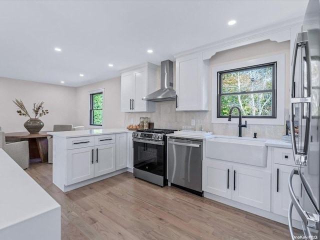 kitchen featuring white cabinetry, sink, wall chimney exhaust hood, stainless steel appliances, and kitchen peninsula