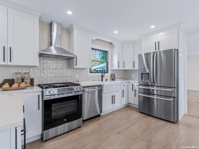 kitchen featuring white cabinets, wall chimney range hood, stainless steel appliances, and light hardwood / wood-style flooring