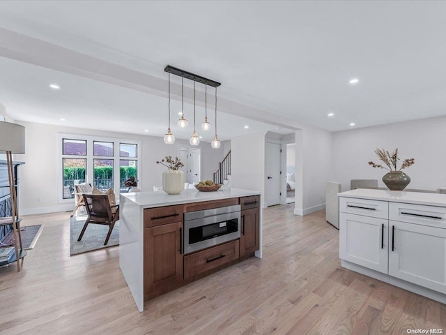 kitchen featuring light wood-type flooring, a kitchen island, pendant lighting, white cabinetry, and stainless steel microwave