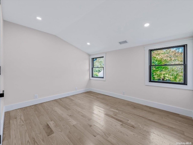 spare room with light wood-type flooring, lofted ceiling, and a healthy amount of sunlight