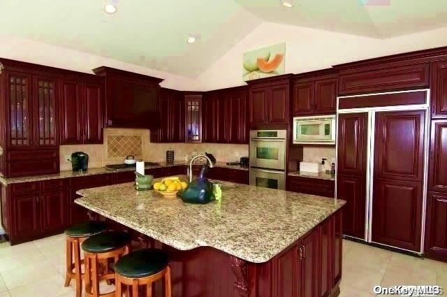 kitchen featuring built in appliances, light stone counters, a center island with sink, and lofted ceiling