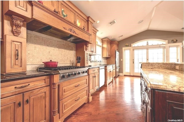 kitchen featuring lofted ceiling, backsplash, dark wood-type flooring, dark stone countertops, and appliances with stainless steel finishes