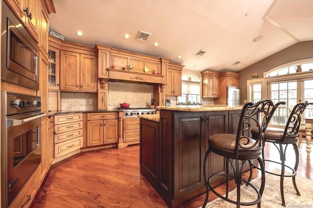 kitchen with light stone countertops, stainless steel appliances, dark wood-type flooring, a kitchen island, and lofted ceiling