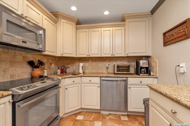 kitchen featuring light stone countertops, backsplash, stainless steel appliances, sink, and cream cabinetry