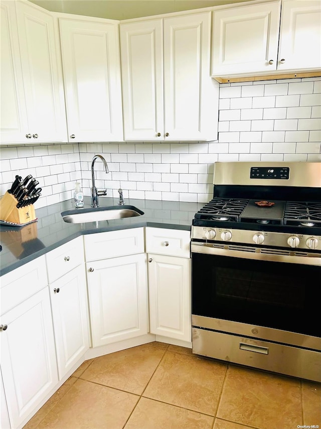 kitchen with white cabinets, sink, gas range, light tile patterned floors, and tasteful backsplash