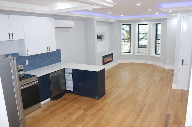 kitchen featuring stainless steel appliances, a wall mounted air conditioner, light hardwood / wood-style flooring, backsplash, and white cabinets