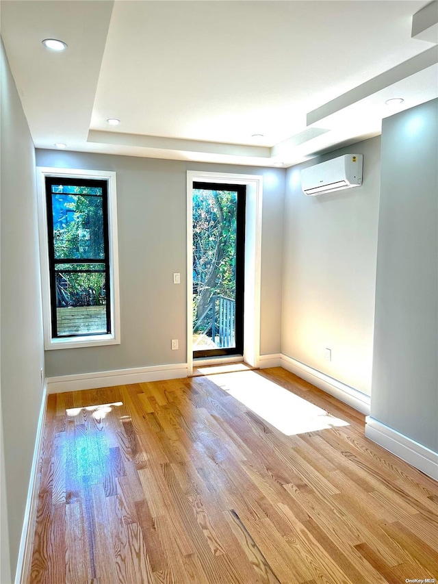 unfurnished room featuring light hardwood / wood-style floors, a raised ceiling, and a wall mounted AC