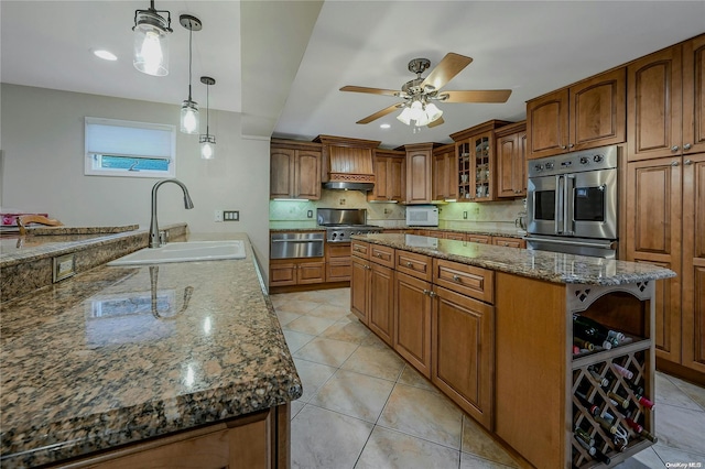 kitchen featuring ceiling fan, sink, dark stone counters, decorative light fixtures, and a kitchen island