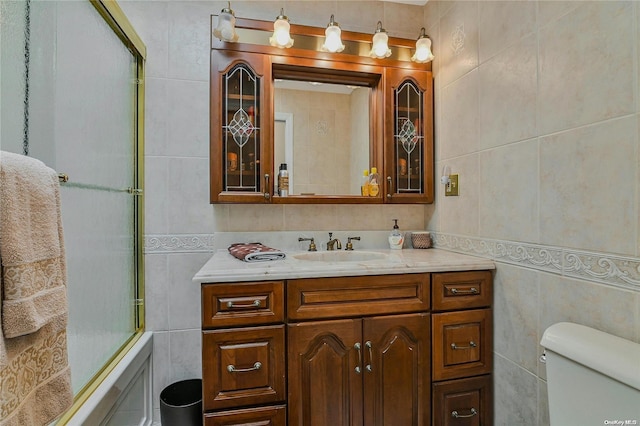 full bathroom featuring combined bath / shower with glass door, vanity, toilet, and tile walls