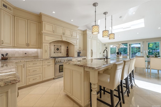 kitchen featuring high end stove, a kitchen island with sink, sink, and cream cabinetry