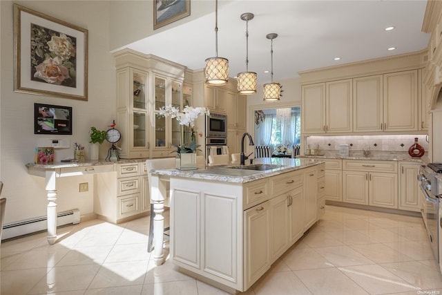 kitchen featuring stainless steel appliances, a baseboard heating unit, pendant lighting, cream cabinets, and an island with sink