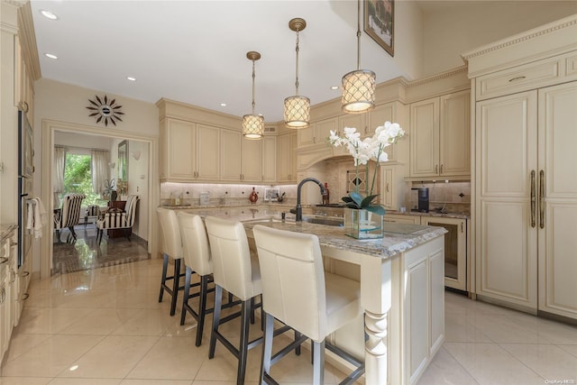 kitchen featuring decorative light fixtures, a center island with sink, tasteful backsplash, and cream cabinets