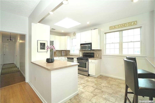 kitchen featuring white cabinetry, light hardwood / wood-style flooring, backsplash, kitchen peninsula, and appliances with stainless steel finishes