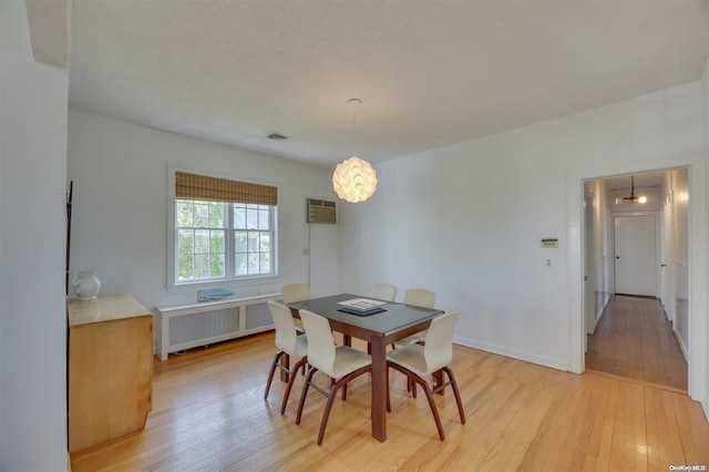 dining space featuring a wall mounted air conditioner, light wood-type flooring, and radiator heating unit