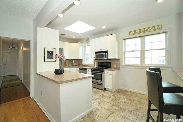 kitchen featuring white cabinets, light wood-type flooring, kitchen peninsula, and appliances with stainless steel finishes