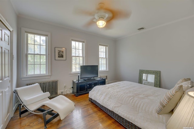 bedroom with radiator, ceiling fan, light hardwood / wood-style floors, and multiple windows