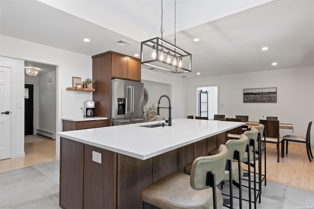 kitchen with a baseboard heating unit, hanging light fixtures, sink, an island with sink, and stainless steel fridge with ice dispenser