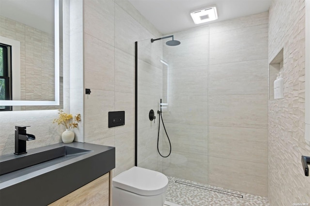 bathroom with a tile shower, vanity, toilet, and tile walls