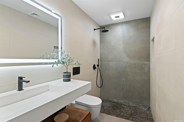 bathroom with sink, toilet, tile walls, and tiled shower