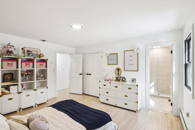 bedroom with a baseboard heating unit, light wood-style flooring, visible vents, and baseboards