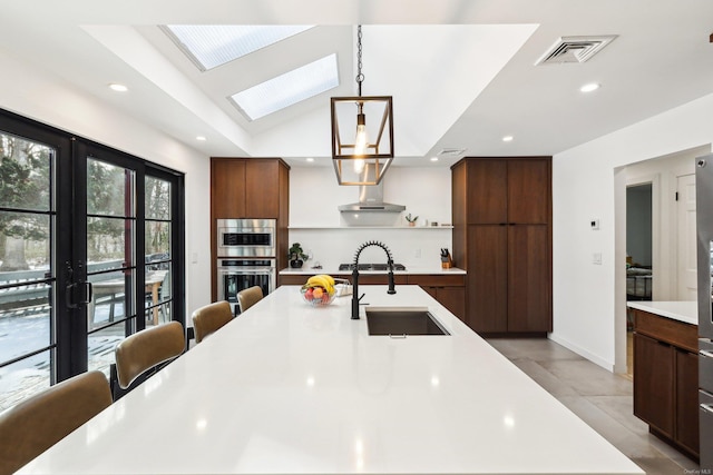 kitchen featuring visible vents, modern cabinets, a sink, wall chimney exhaust hood, and light countertops