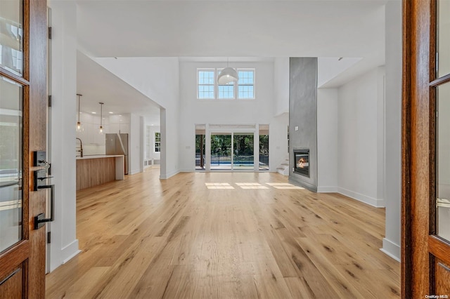 2060 Shipyard Ln, East Marion, NY 11939 - unfurnished living room featuring light wood-type flooring, baseboards, a towering ceiling, and a glass covered fireplace
