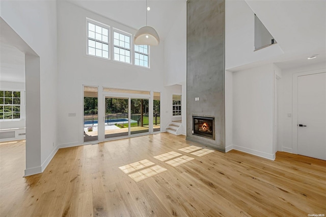 unfurnished living room with a large fireplace, light wood-type flooring, and a high ceiling