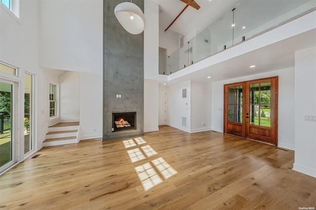 unfurnished living room featuring a high ceiling, light wood-type flooring, french doors, and a healthy amount of sunlight