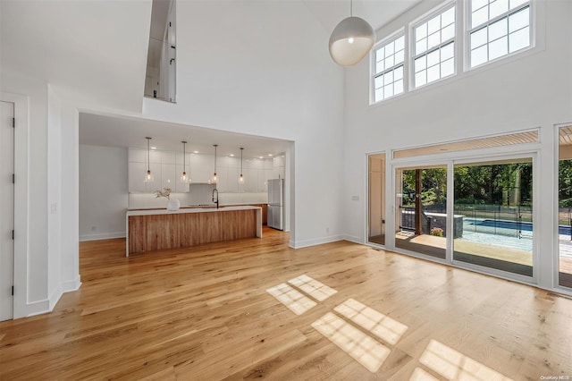 2060 Shipyard Ln, East Marion, NY 11939 - unfurnished living room featuring a towering ceiling, plenty of natural light, baseboards, light wood-style floors, and a sink