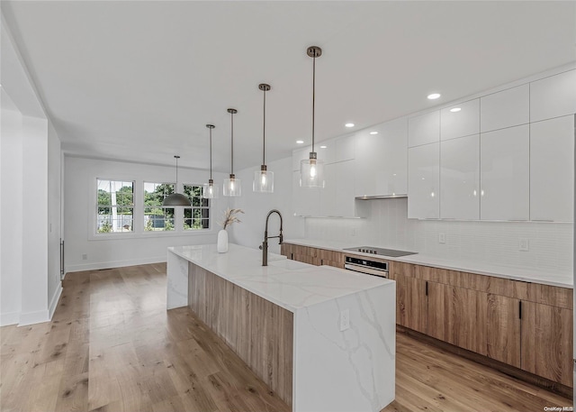 kitchen featuring a large island with sink, hanging light fixtures, light hardwood / wood-style floors, light stone counters, and white cabinetry