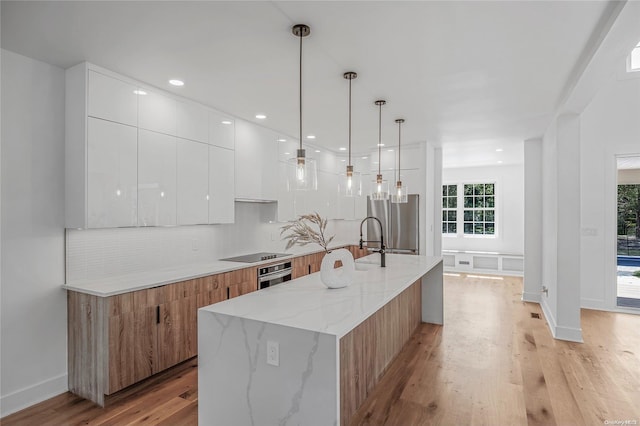 kitchen with white cabinetry, hanging light fixtures, a center island with sink, appliances with stainless steel finishes, and light wood-type flooring