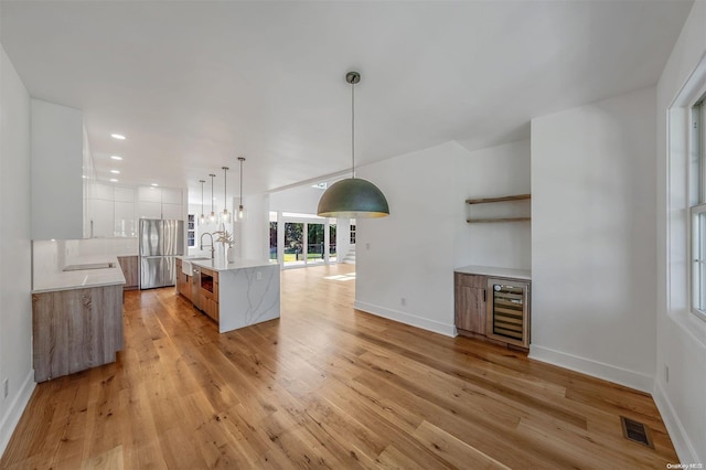 kitchen with a center island with sink, stainless steel refrigerator, light hardwood / wood-style floors, white cabinetry, and beverage cooler