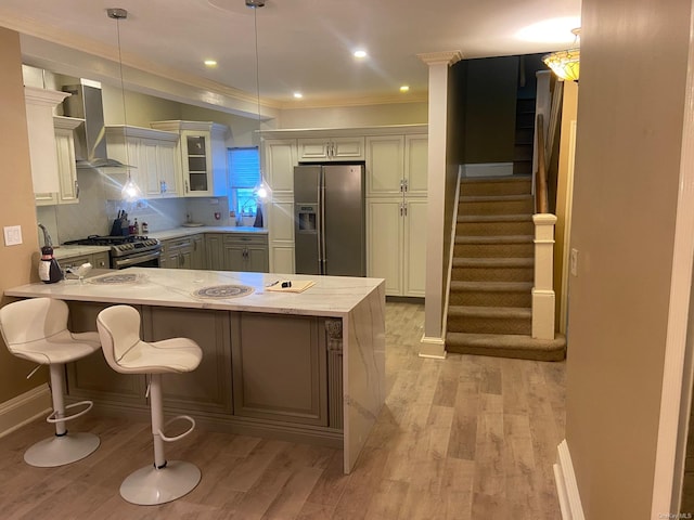 kitchen with wall chimney exhaust hood, kitchen peninsula, light hardwood / wood-style floors, pendant lighting, and appliances with stainless steel finishes