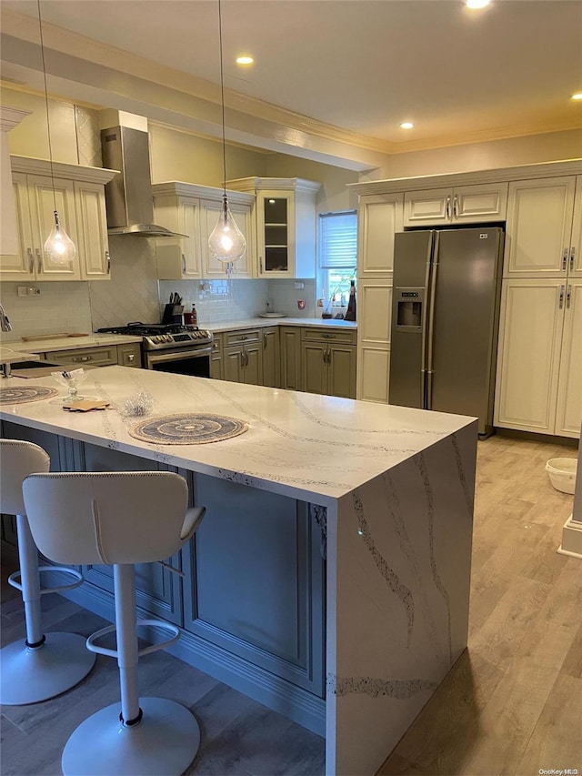 kitchen with wall chimney exhaust hood, hanging light fixtures, stainless steel appliances, a kitchen breakfast bar, and light hardwood / wood-style floors