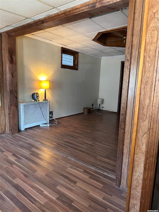 basement with a drop ceiling, dark hardwood / wood-style floors, and radiator