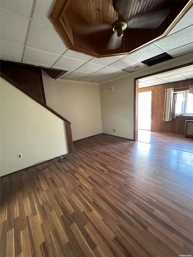 interior space featuring a paneled ceiling, wooden walls, and dark wood-type flooring