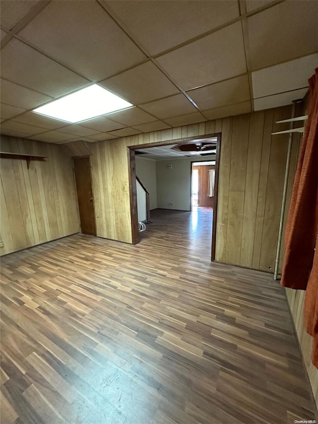 unfurnished room with hardwood / wood-style floors, a drop ceiling, and wooden walls